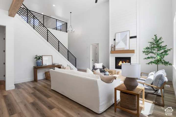 High ceilings with an exposed wood beam, wood-finish flooring, a contemporary fireplace with a shiplap surround and wood mantel, and a staircase featuring black horizontal iron railings