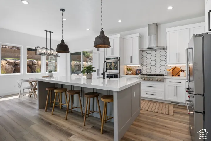 Gourmet kitchen with wood-finish flooring, white cabinetry, a large kitchen island with counter seating, stainless steel appliances, and a hexagonal tile backsplash