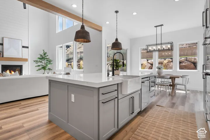Vaulted ceiling with exposed beam, fireplace with shiplap surround, kitchen island with built-in farmhouse sink, stainless steel appliances, and recessed lighting