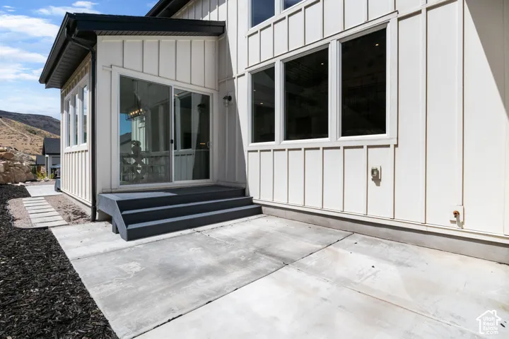Board and batten siding, multiple large windows, dark-toned stairs, concrete patio, and a sliding glass door
