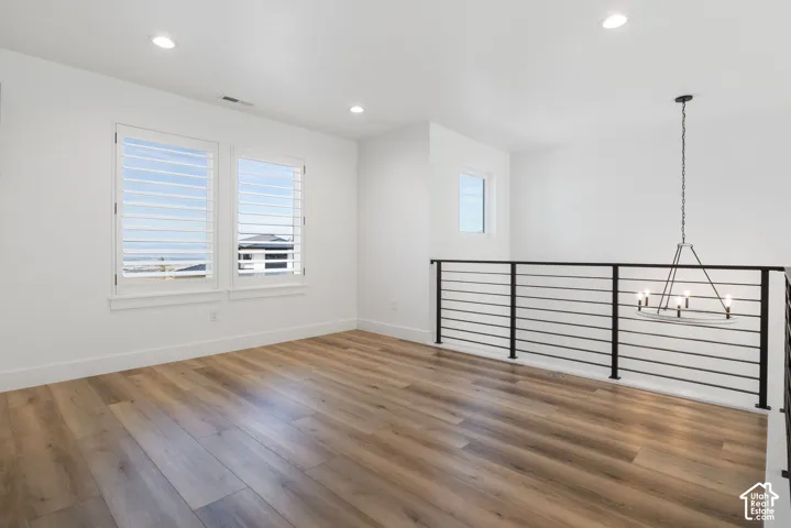 Open loft area with wood-finish flooring, recessed lighting, and a contemporary chandelier