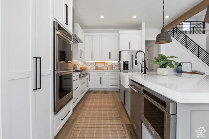 Gourmet kitchen with white cabinetry, stainless steel appliances, hexagon tile backsplash, and an expansive island with a farmhouse sink