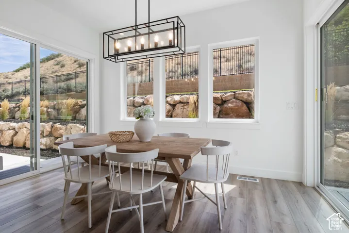 Wood-finish flooring, white walls, and a linear black chandelier illuminate the dining space