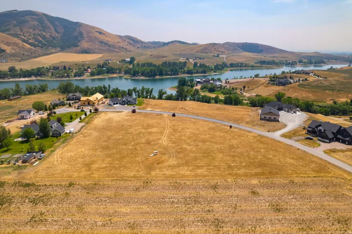 Expansive undeveloped lot featuring a paved road, surrounded by residential properties and natural landscaping