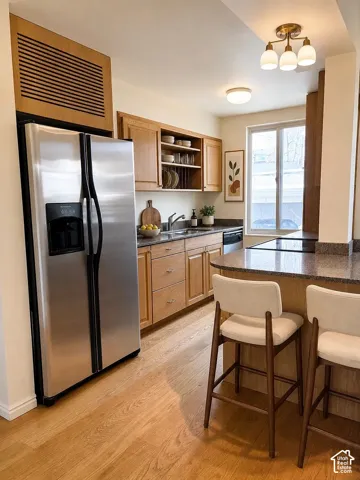 Stainless steel refrigerator, wood-finish flooring, wood cabinetry, stone countertops, and a built-in breakfast bar