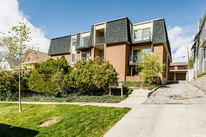 Brick exterior with a mansard roof, multiple balconies, a front lawn, and an asphalt driveway