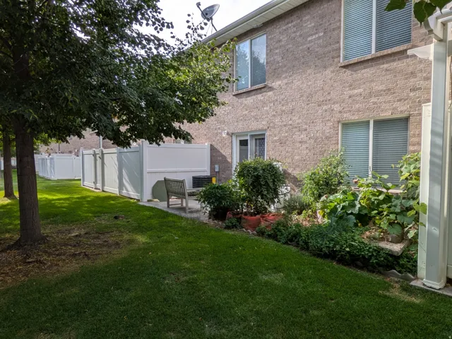 Brick exterior with multiple windows, a manicured lawn, and a white privacy fence