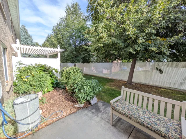 Paved patio area, white pergola structure, mature trees, manicured lawn, and privacy fencing