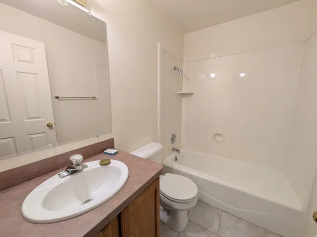 Bathroom featuring a built-in vanity with an integrated sink, a full-width mirror, a shower/tub combination, and tiled flooring