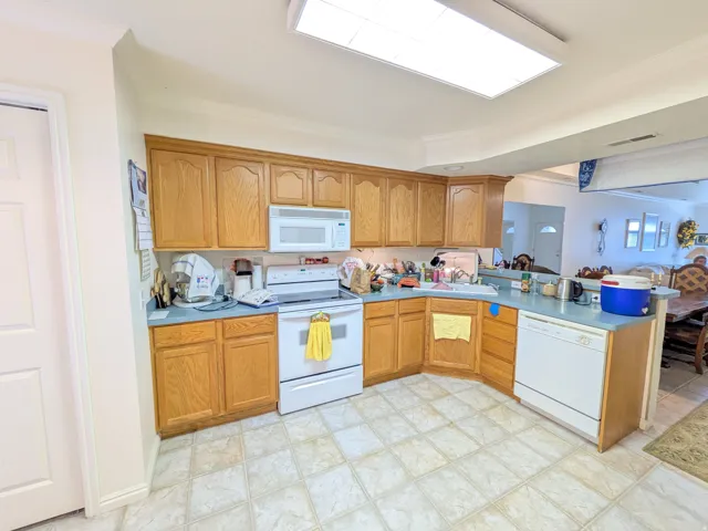 U-shaped kitchen featuring wood cabinetry, white appliances, light blue countertops, and tiled flooring