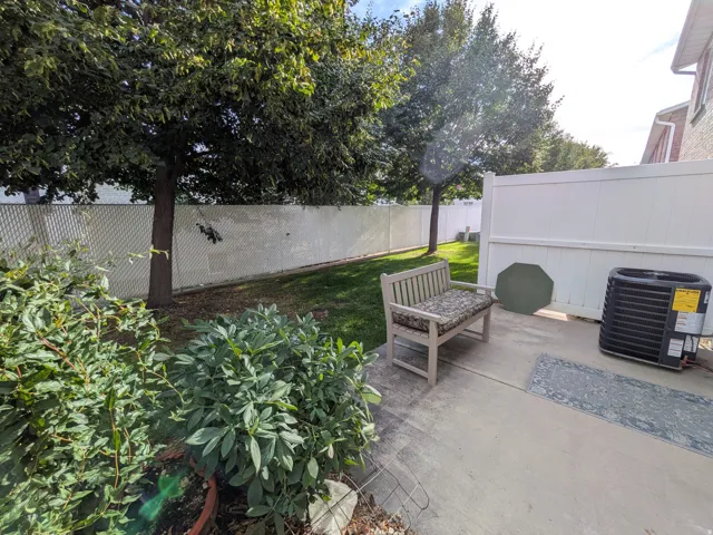 Concrete patio area featuring a white privacy fence, mature trees, and landscaping
