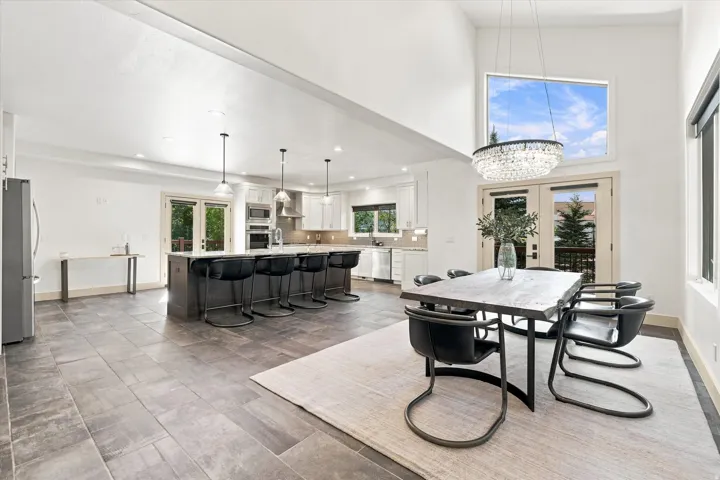 Open-concept living space featuring high ceilings, a large kitchen island with seating, pendant lighting, stainless steel appliances, and French doors