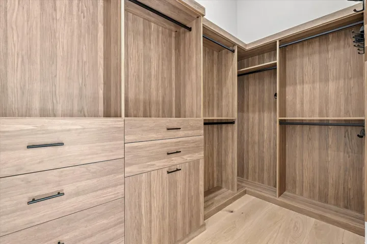 Custom closet system featuring wood-finish cabinetry, integrated shelving, dark hardware, and hanging rods