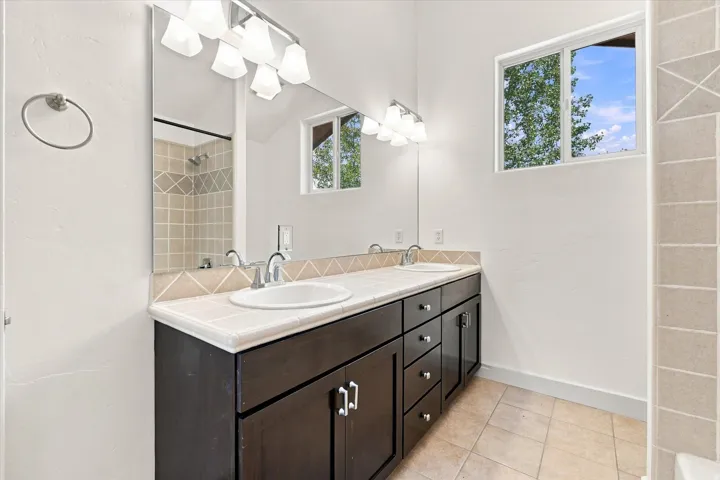 Dual vanity with dark wood-finish cabinetry, tile countertop, and matching tile flooring