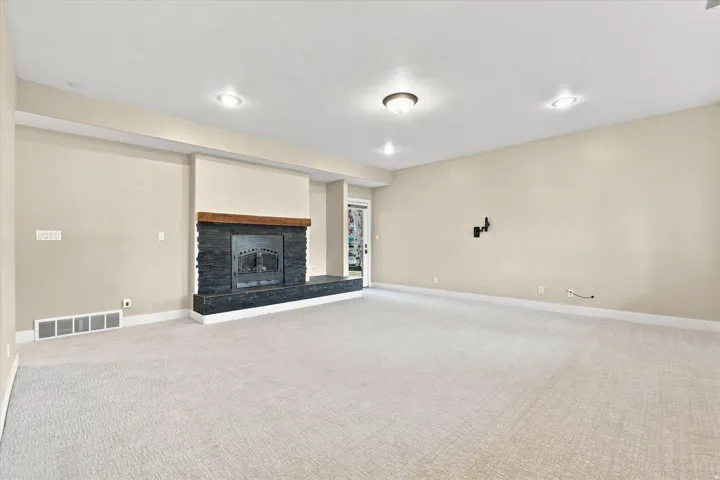 Spacious interior with neutral-toned walls, recessed lighting, and a prominent fireplace featuring a dark stone surround and a wood mantel