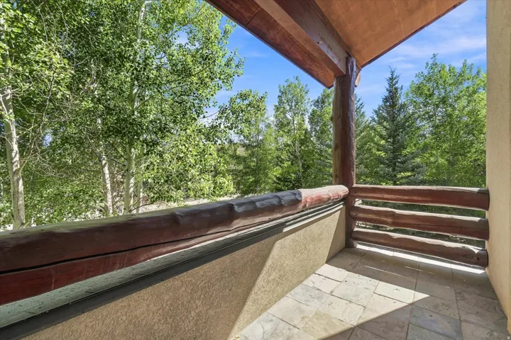 Balcony featuring natural wood railing and support beams, textured exterior walls, and stone tile flooring