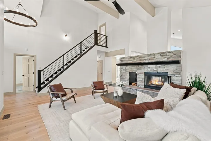 Soaring ceilings, stone-clad fireplace, wood-finish flooring, contemporary open-tread staircase with metal railing, and overhead wood beams