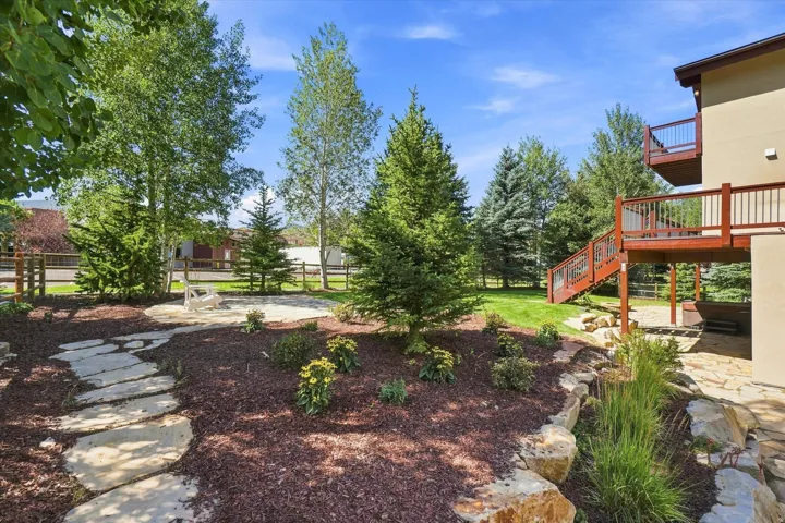 Tiered landscaping with natural stone retaining walls, flagstone steps, extensive mulch beds, and mature trees