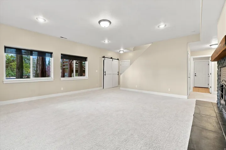 Spacious recreation room with recessed ceiling lighting, large windows with black-framed panes flooding the space with natural light, neutral carpet flooring, and direct access to adjacent areas through multiple doorways