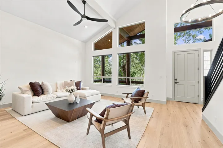 Vaulted ceiling with exposed beam, large picture windows, wood-finish flooring, staircase with metal railing, and a contemporary ceiling fan