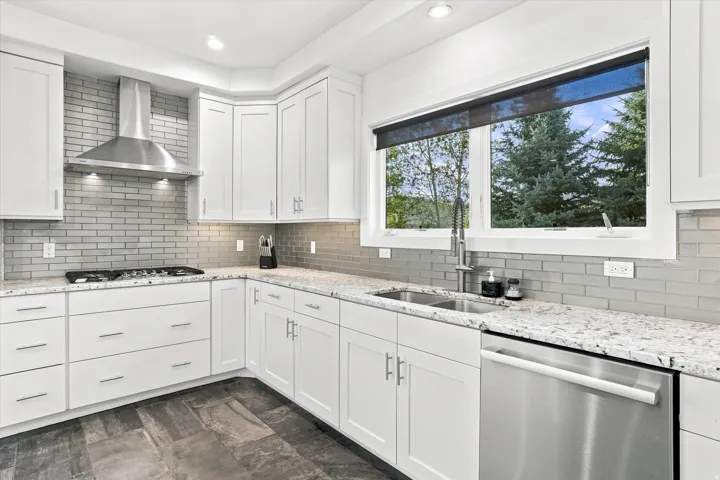 White shaker cabinetry, light-toned granite countertops, stainless steel appliances, grey subway tile backsplash, and dark-toned tile flooring