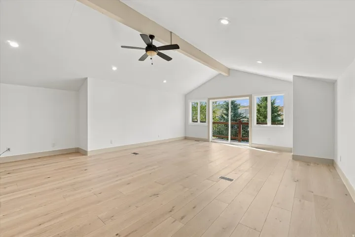 Vaulted ceiling with exposed beam, recessed lighting, wood-finish flooring, ceiling fan, and sliding glass door leading to an outdoor deck