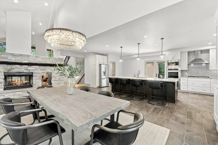 Stone-clad fireplace with hearth, kitchen island with seating, stainless steel appliances, white cabinetry, and large format tile flooring