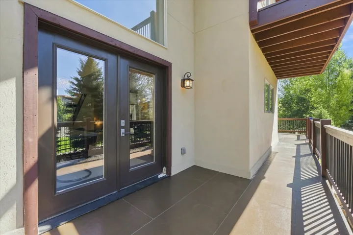 Exterior patio featuring dual French doors, a built-in outdoor wall sconce, and a wood-finish railing