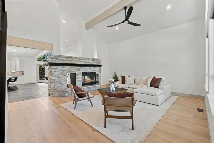 Vaulted ceiling, stone-clad fireplace with mantel, light wood-finish flooring, recessed lighting, and a contemporary ceiling fan