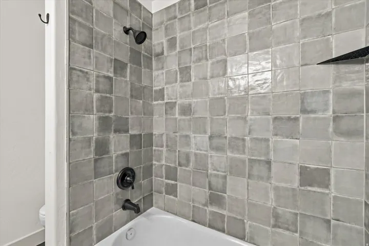 Bathtub with dark-toned fixtures and varied-shade square tile surround