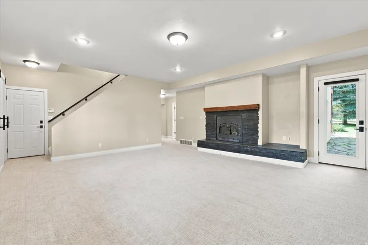 Spacious room featuring a stone fireplace with a wood mantle, neutral carpeting, recessed lighting, and an exterior door with a glass panel