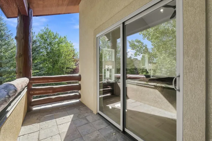 Outdoor balcony with log railing, natural wood ceiling, stone tile flooring, and large sliding glass doors