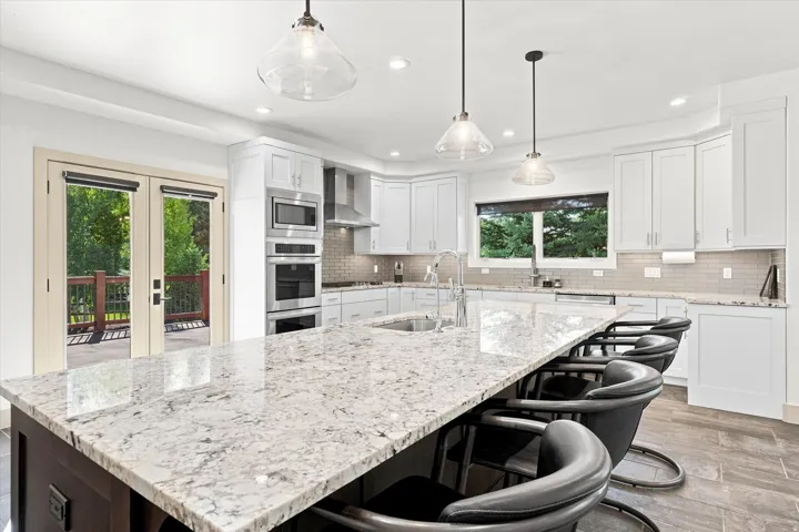 Spacious kitchen featuring an expansive island with a light-toned countertop, white cabinetry, integrated stainless steel appliances, and French doors opening to an outdoor deck