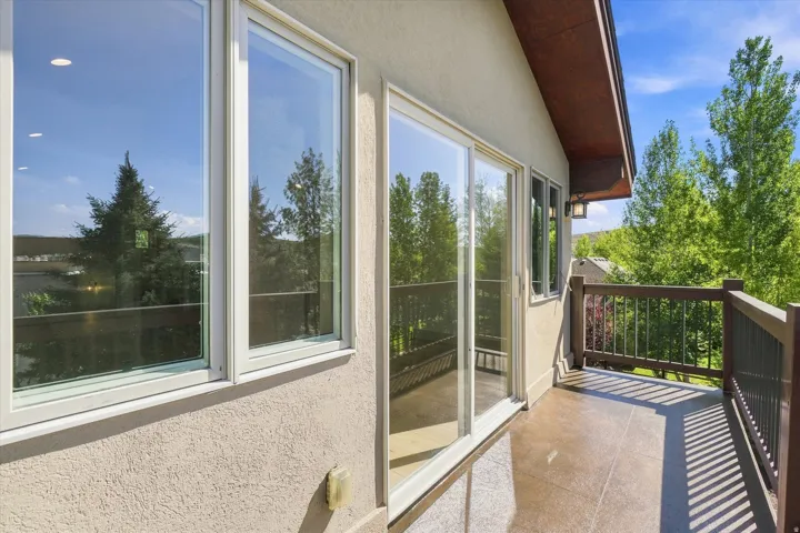 Expansive balcony featuring a textured concrete surface, wood-toned railings, and a sliding glass door