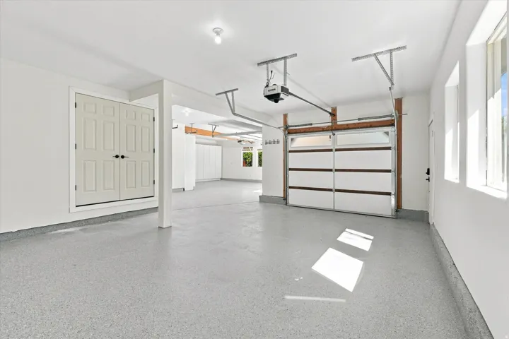 Spacious garage featuring a finished epoxy floor, panel garage door with upper glass inserts, recessed lighting, and dual windows providing natural illumination