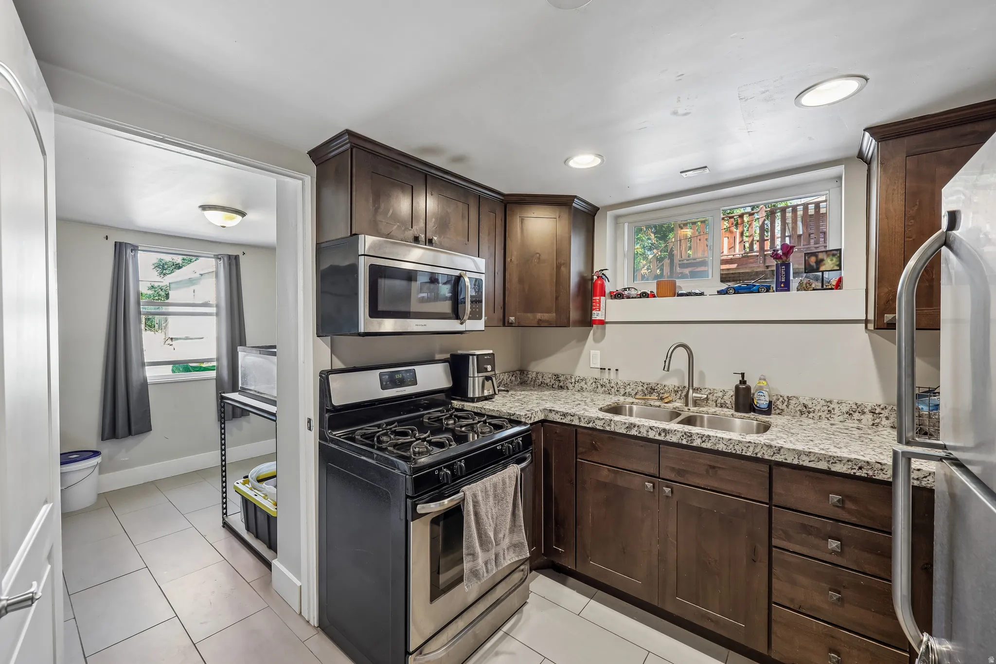 Kitchen featuring wood-finish cabinetry, granite-style countertops, stainless steel appliances, a dual-basin sink, and recessed lighting