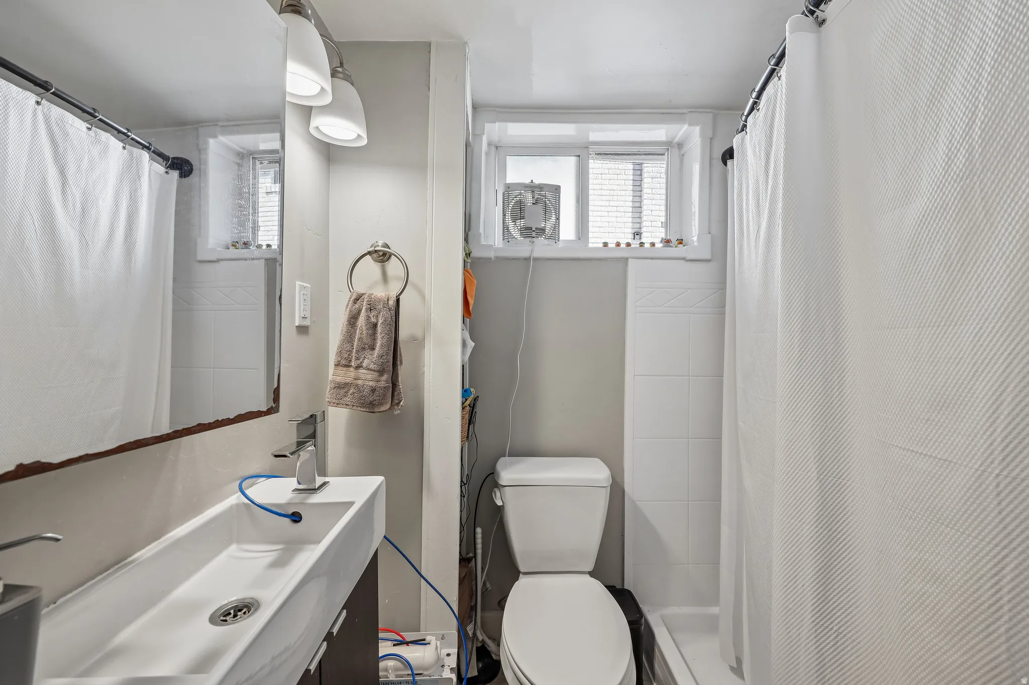 Modern trough sink with a single-handle faucet, wall-mounted vanity lighting, and a window with privacy blinds