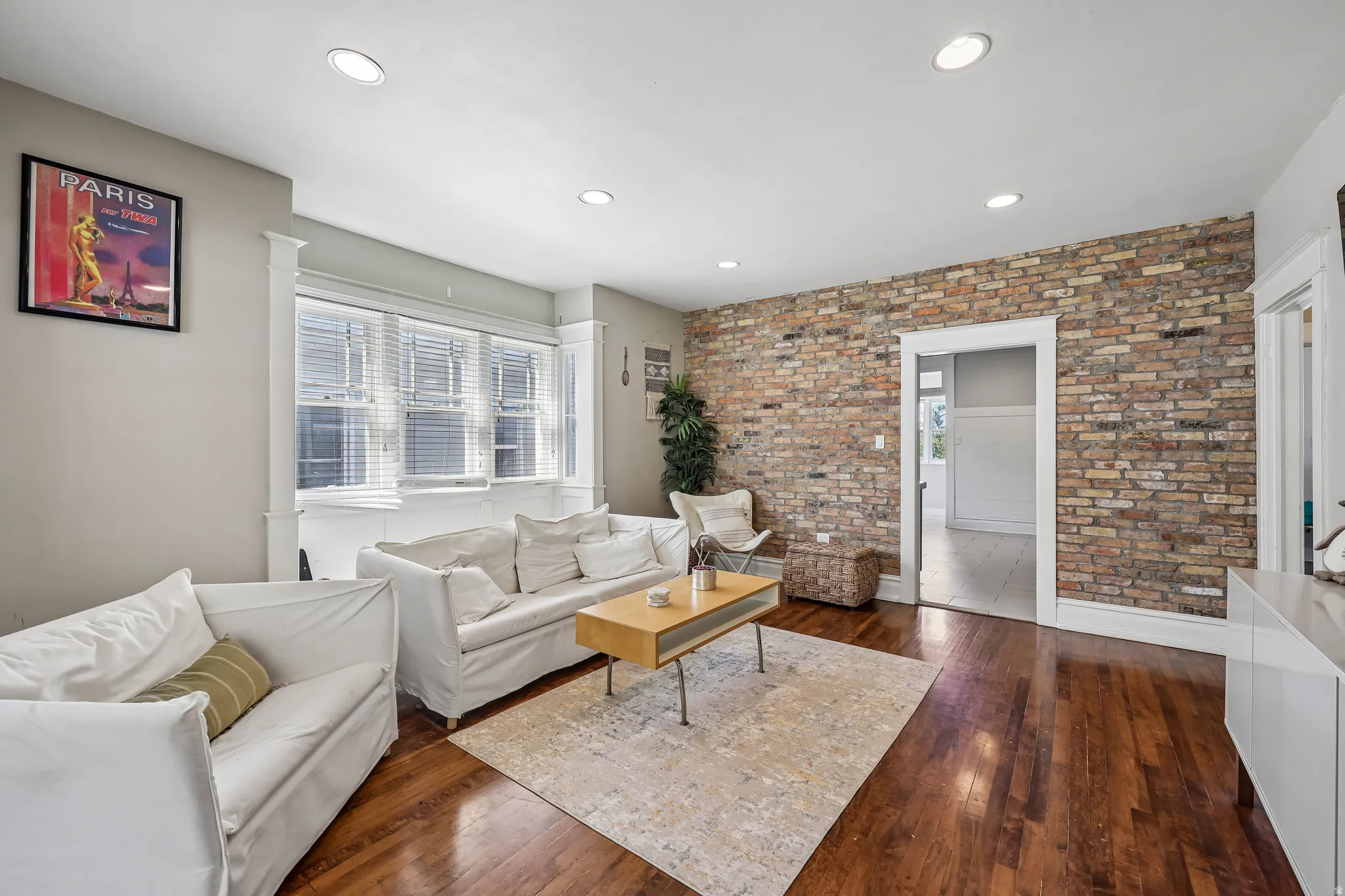 Exposed brick accent wall, wood-finish flooring, recessed lighting, and a bay window with window treatments