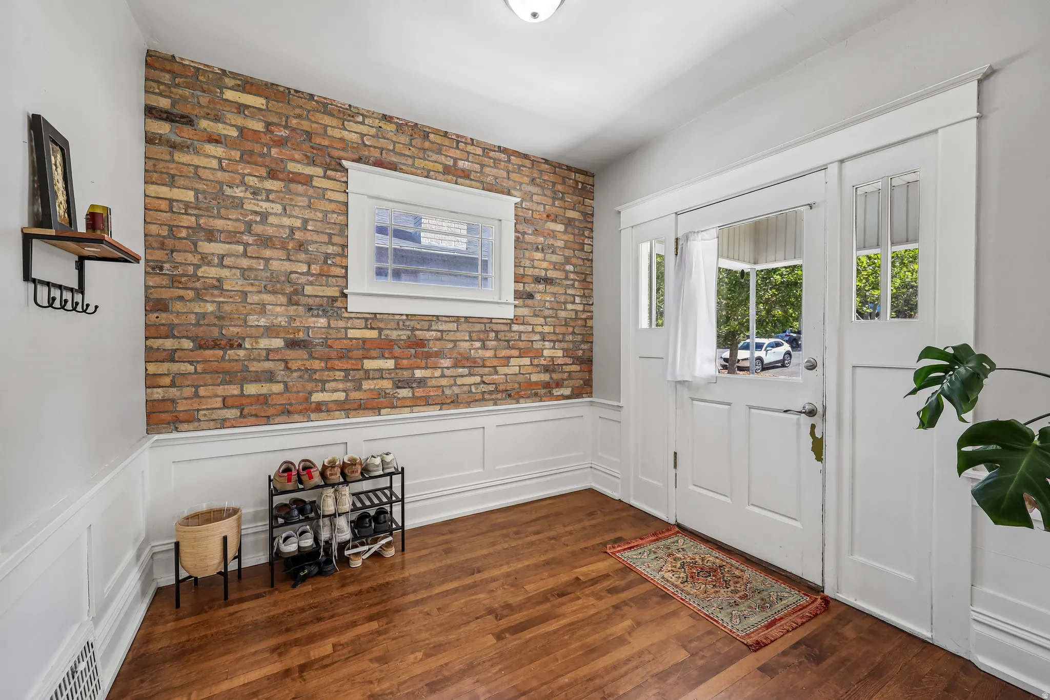 Hardwood flooring, exposed brick wall, white wainscoting, transom windows, and a white paneled entry door
