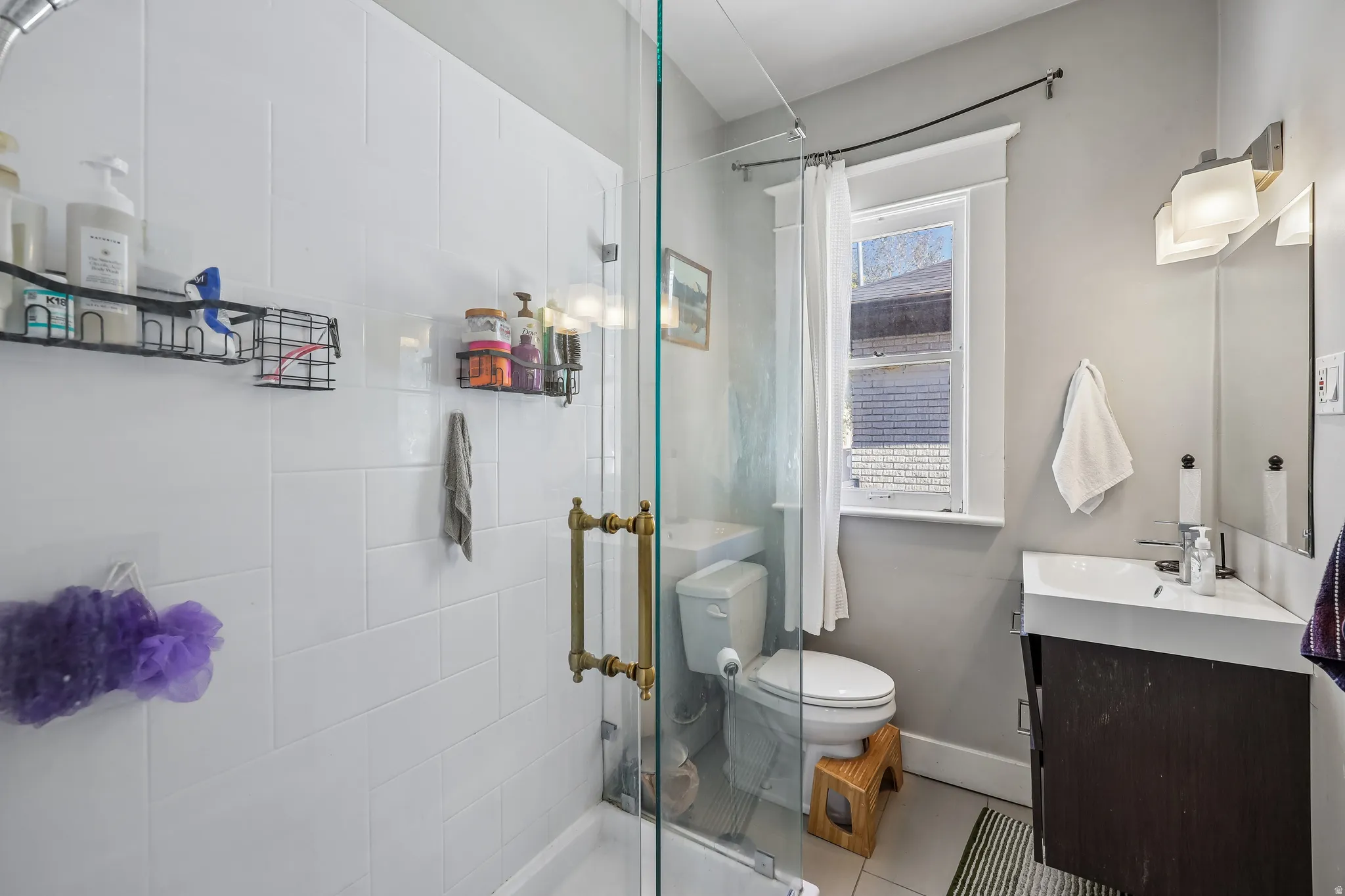 Glass-enclosed shower with subway tile surround, floating vanity with integrated sink, and wall-mounted lighting