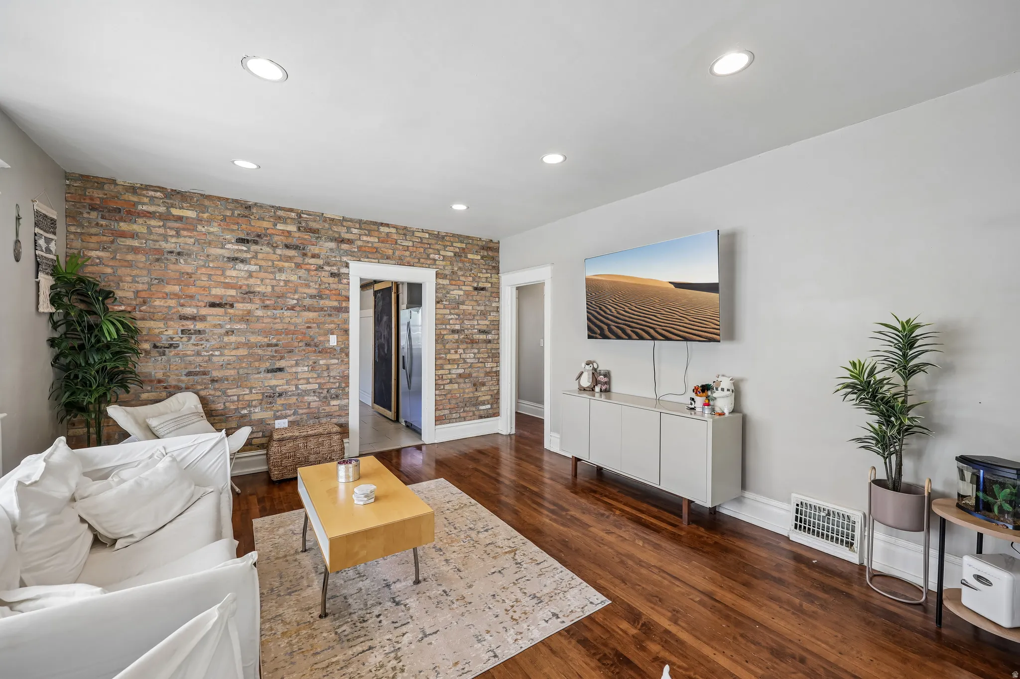 Exposed brick accent wall, recessed ceiling lighting, wood-finish flooring, white trim, and light gray wall paint