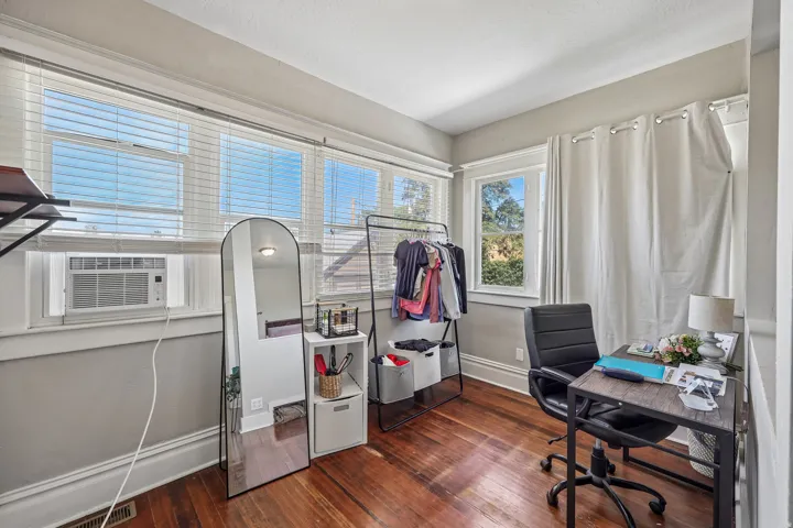Hardwood flooring, multiple windows with blinds, gray wall paint, white trim, and a window-mounted air conditioning unit