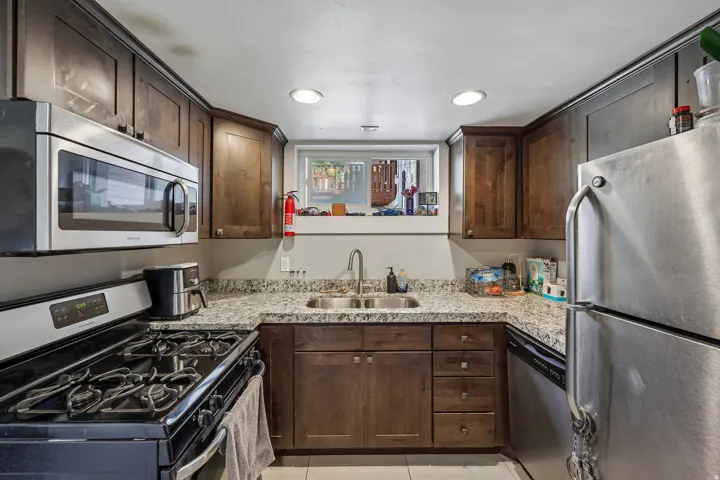 Modern kitchen featuring stainless steel appliances, granite countertops, recessed lighting, and wood-finish cabinetry