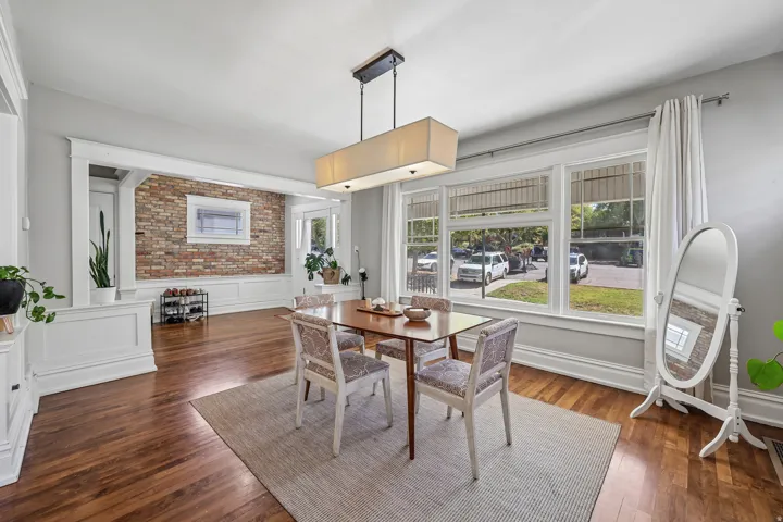 Hardwood flooring, exposed brick accent wall, white trim work, multiple windows, and a modern rectangular light fixture