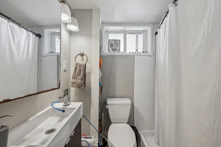 Modern trough sink with a single-handle faucet, wall-mounted vanity lighting, and a window with privacy blinds