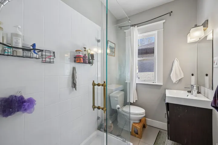 Glass-enclosed shower with subway tile surround, floating vanity with integrated sink, and wall-mounted lighting