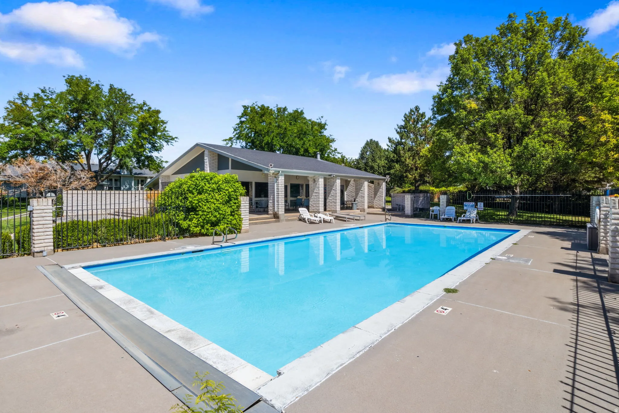 Expansive outdoor pool with a concrete surround, black metal fencing, and Clubhouse