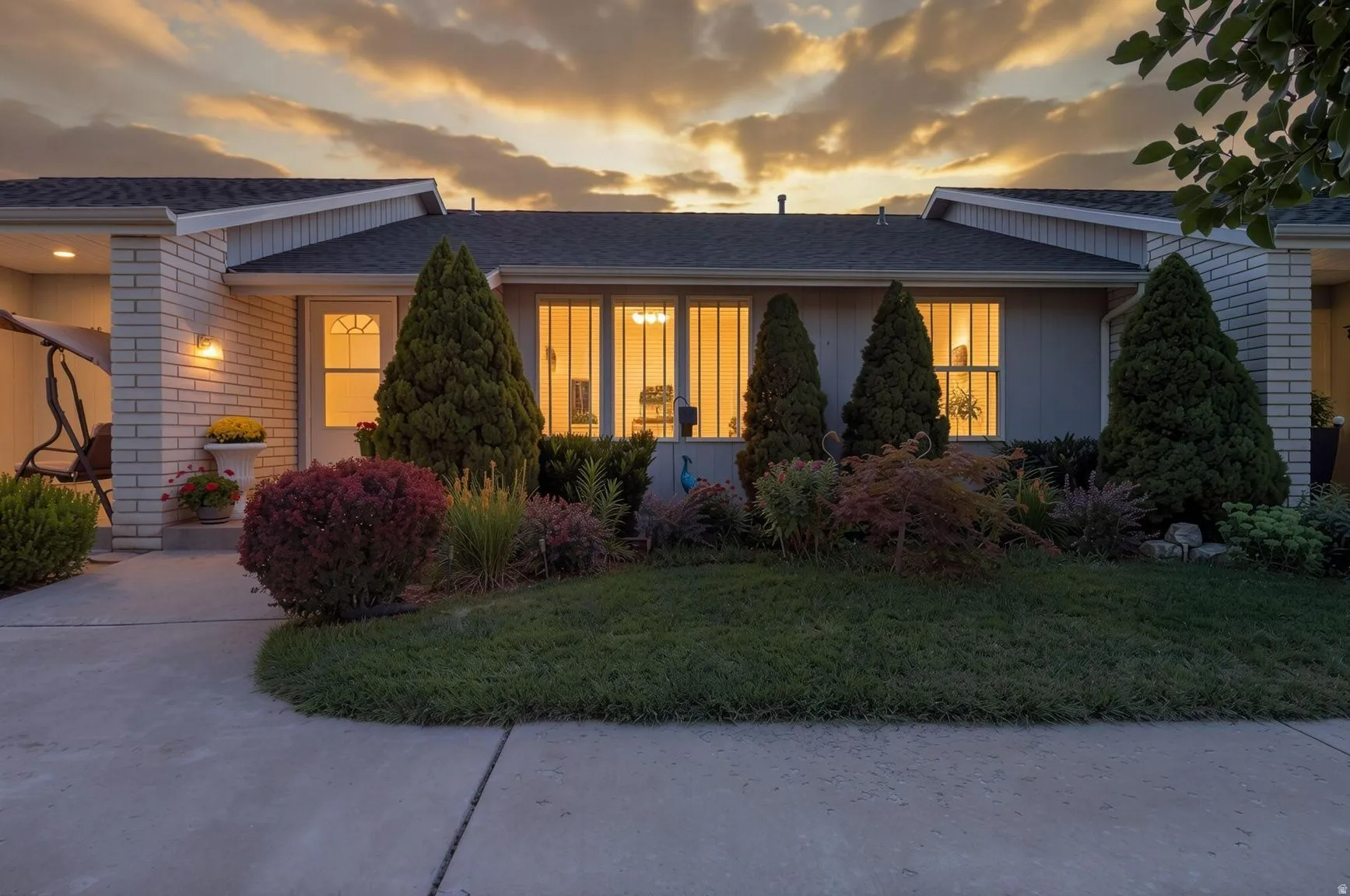 Single-story residence featuring a covered entry porch, white brick exterior accents, a well-maintained lawn, and established landscaping