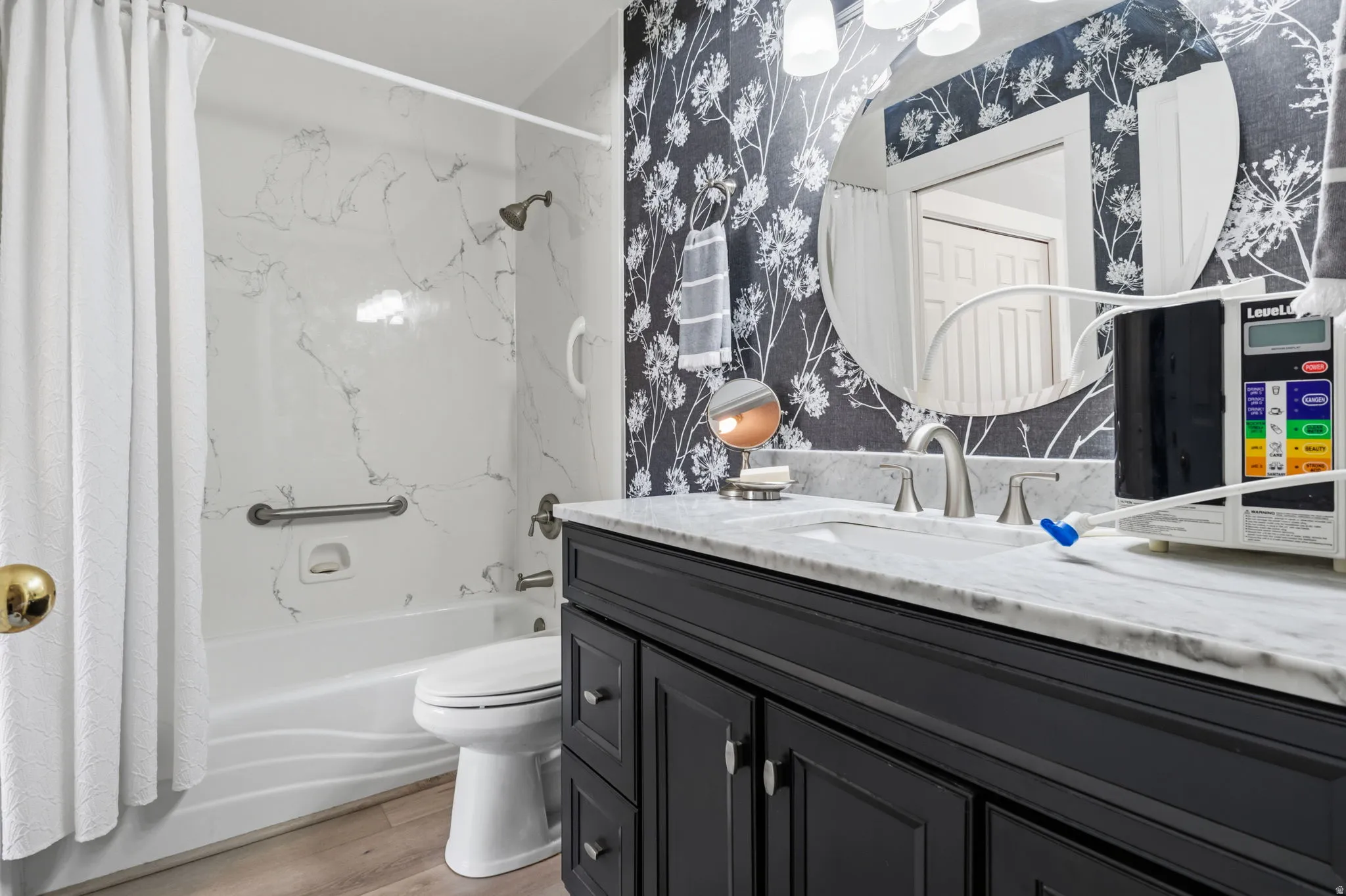 Tub/shower combination with a marble-patterned surround, dark-finish vanity with a light-tone countertop, and Gray LVP flooring