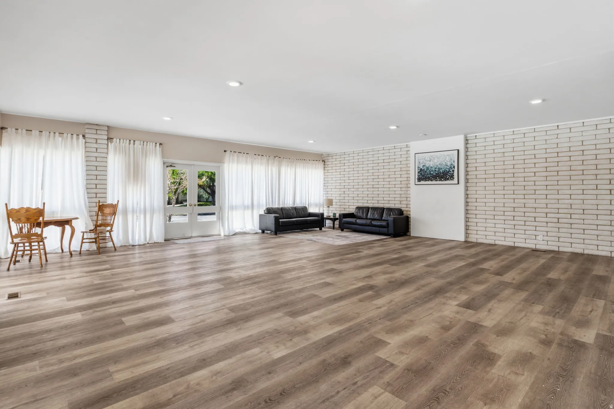 Expansive room featuring wood-finish flooring, white brick accent walls, recessed lighting, and multiple French doors